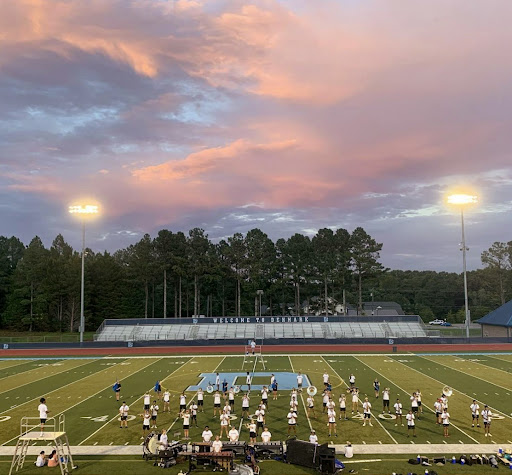 The marching band practices their formations during a beautiful sunset.