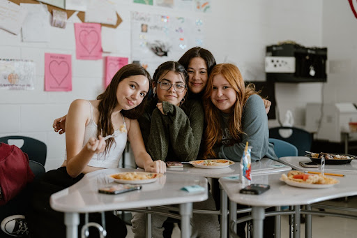 Miranda Meano, Camila Delgado, Lilah Martens, and Caitlyn Jeffrey huddle together, sharing in Thanksgiving spirit and food at Newspapers gathering.